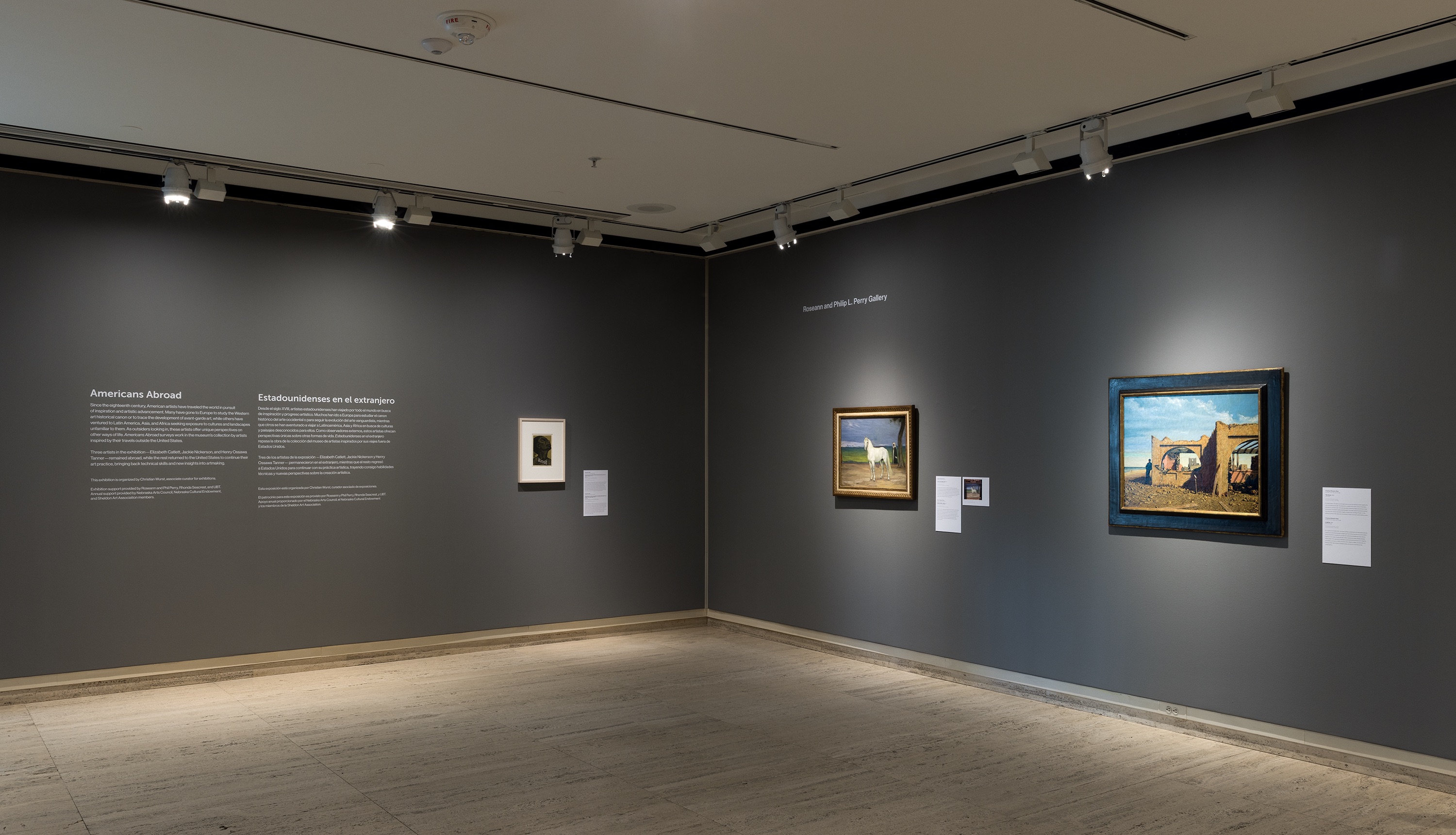 Museum gallery with framed artwork displayed on dark gray walls under spotlights.