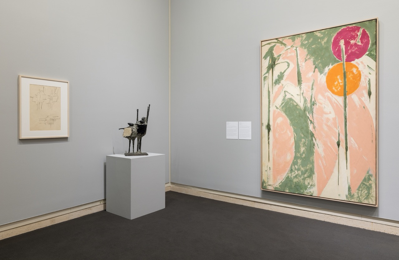 Art gallery display with abstract painting, framed sketch, and small metal sculpture on a pedestal.