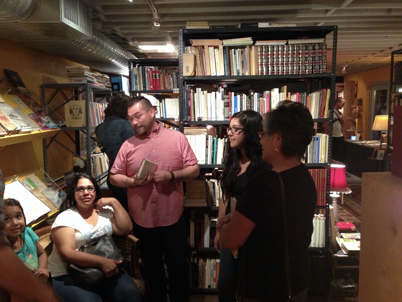 Group of people talking and browsing books in a cozy, brightly lit bookstore.