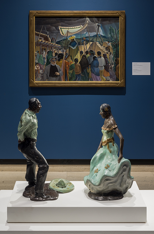 Two colorful ceramic sculptures of a man and woman in traditional attire, with a framed painting behind.