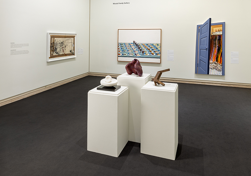 Art gallery with sculptures on white pedestals and colorful paintings on cream walls.