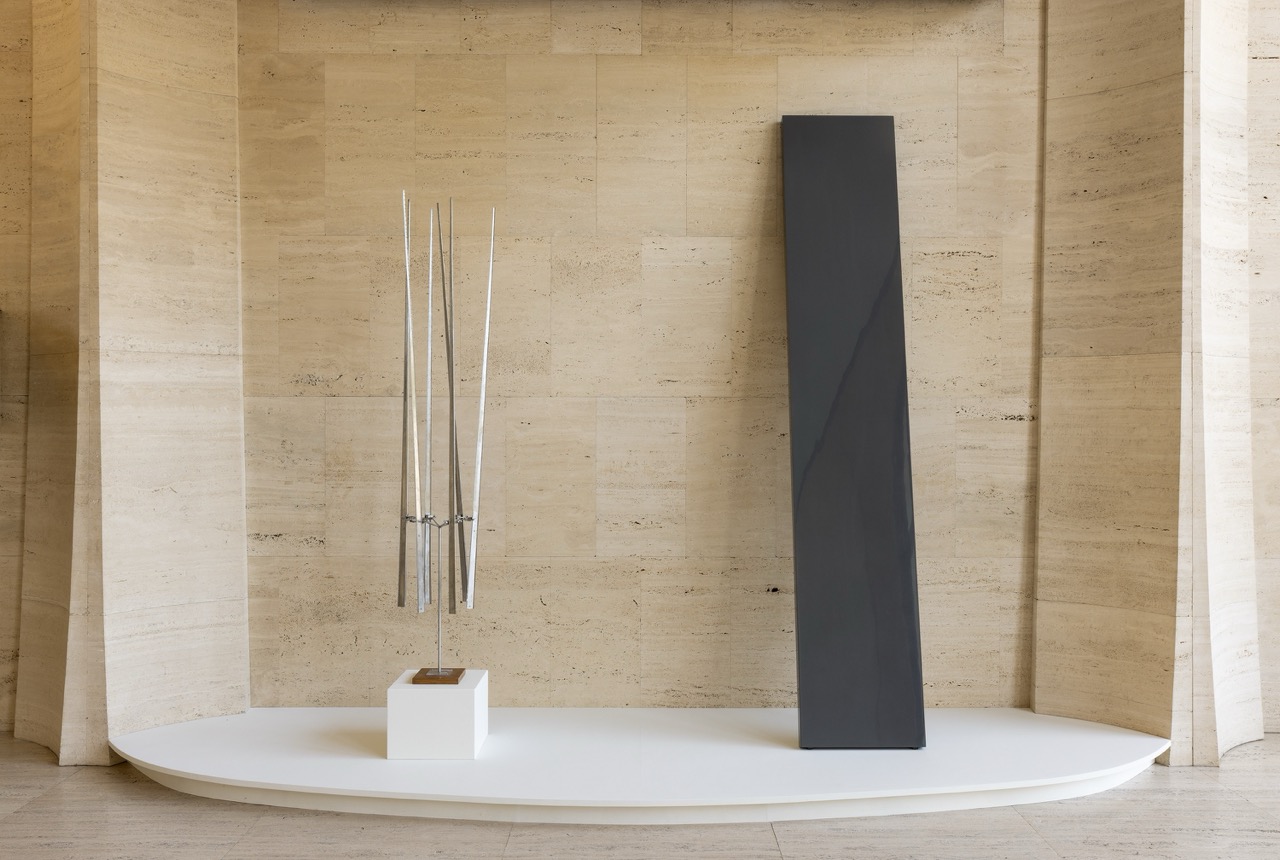 Sculptural artworks on a modern platform against a beige marble wall.