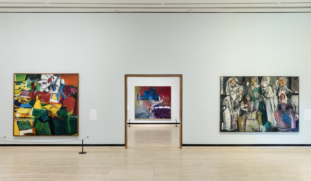 Colorful abstract paintings and a group portrait displayed in a modern, spacious gallery room.