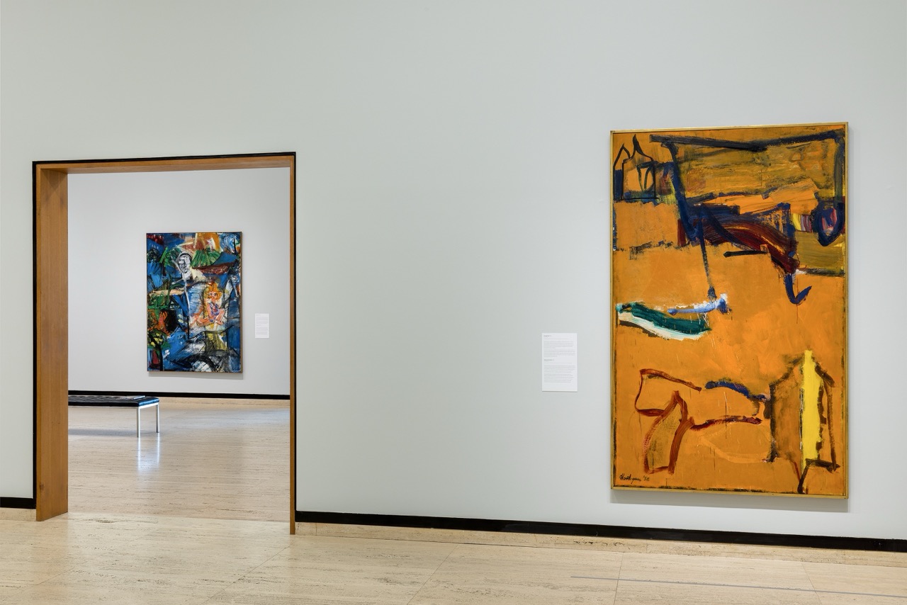 Colorful abstract paintings displayed in a modern art gallery with neutral walls and wooden frames.