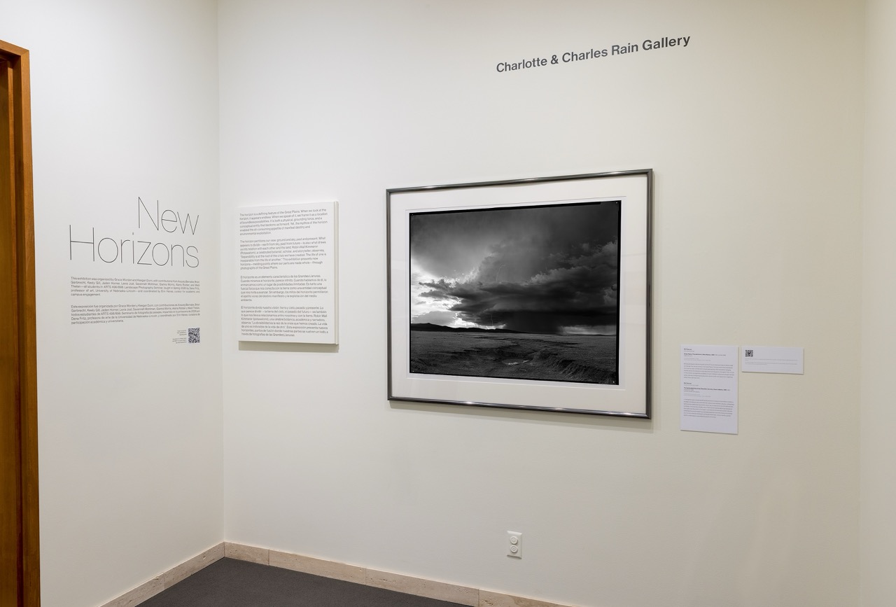 Black-and-white landscape photograph hangs on a gallery wall with accompanying text panels nearby.