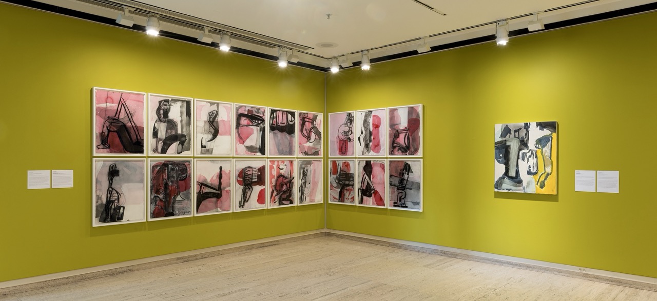 Art gallery display with framed abstract paintings on bright green walls, showcasing pink, black, and yellow tones.