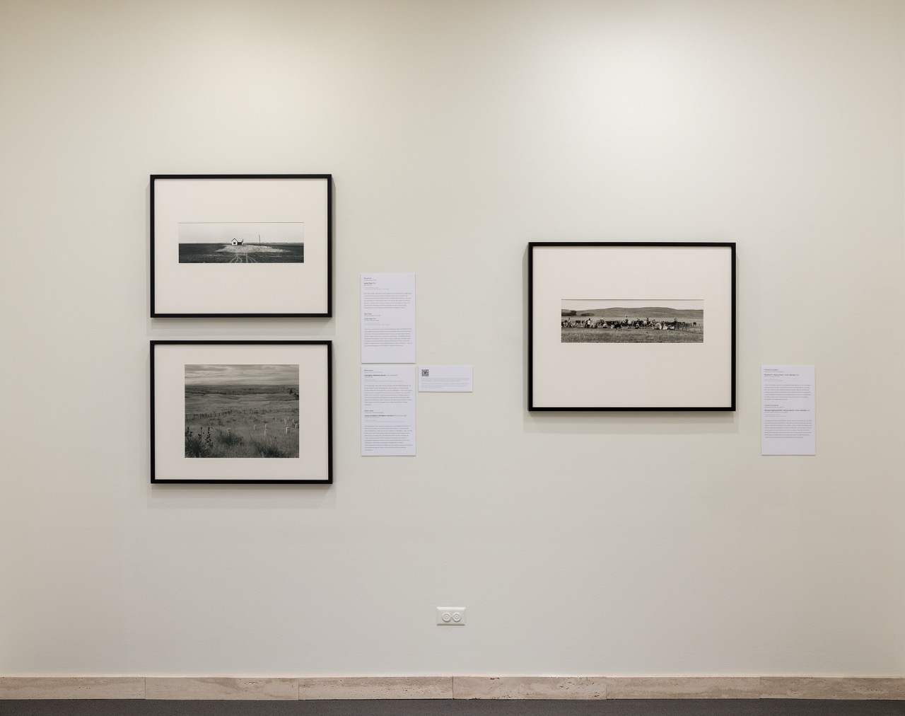 Framed black-and-white photographs displayed on a neutral gallery wall with informational plaques.
