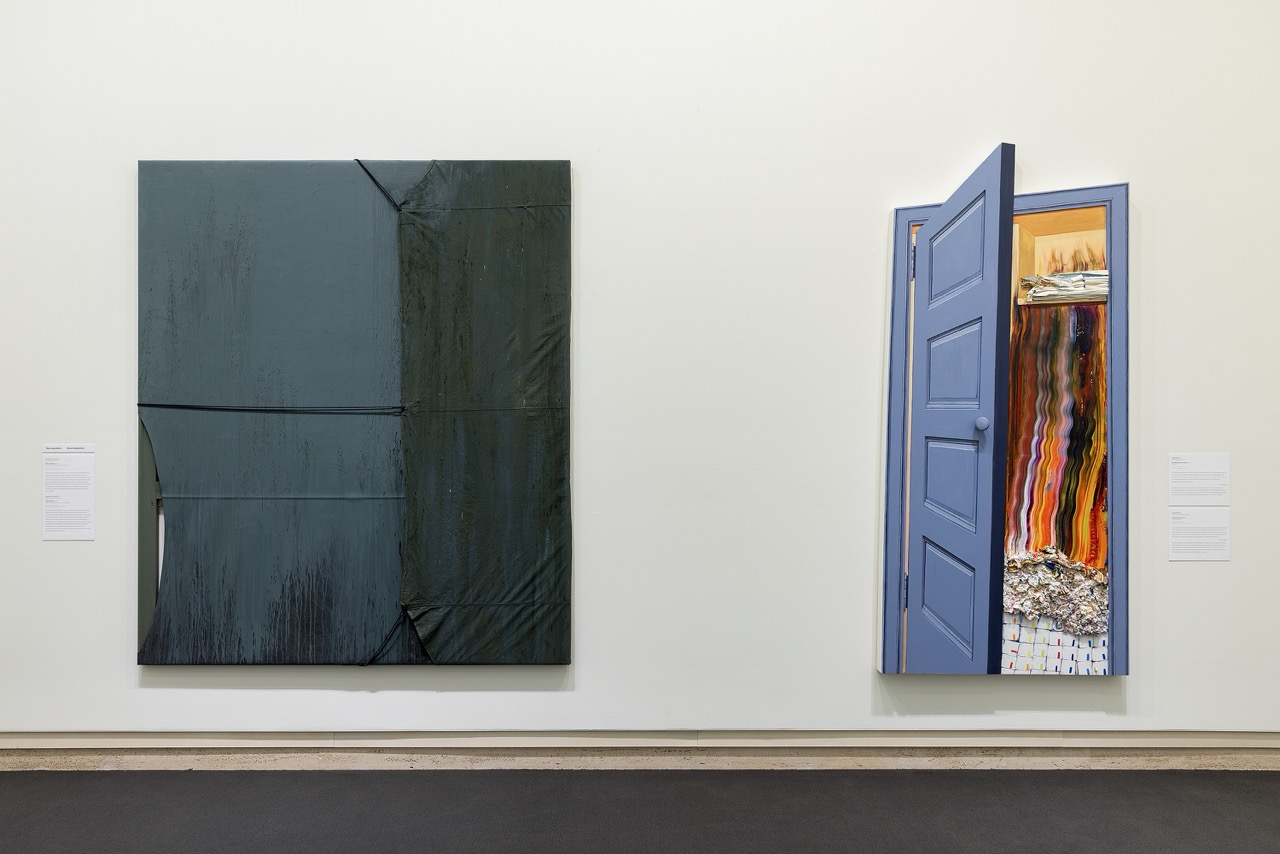 Two artworks on a white wall: a textured dark canvas and a blue door framing colorful abstract art.