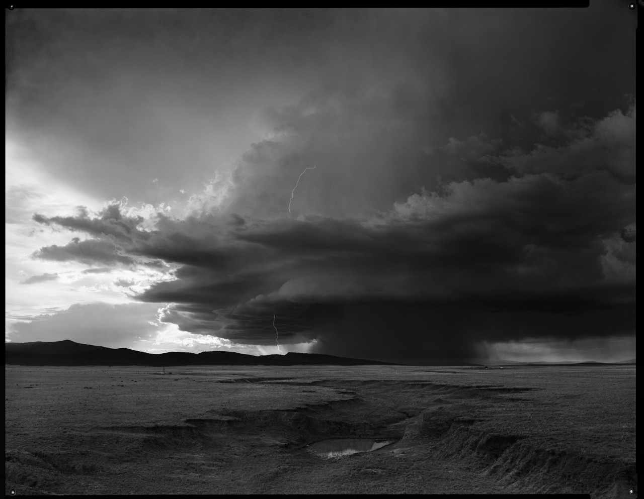 Dark storm clouds over open plains with lightning striking in the distance. Black and white photograph.