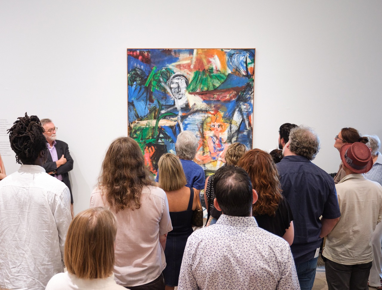 A group of people gathered in front of a colorful abstract painting in a gallery setting.