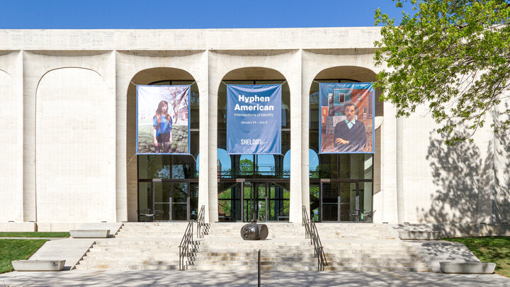 East entrance of Sheldon Museum of Art on a sunny day with banners promoting the exhibition "Hyphen American"